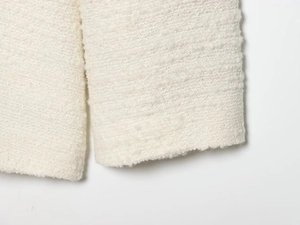 Close-up of white tweed jacket cuff showing premium textured fabric and weaving details