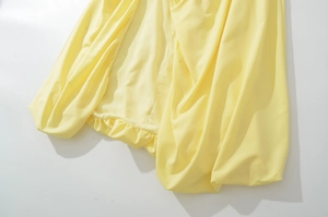 Detail view of bright yellow strapless dress showing silky fabric and ruffled hemline