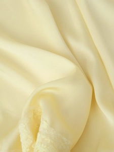 Détail du tissu en satin jaune pâle avec broderie de dentelle florale et texture lisse