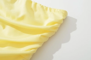 Detailed close-up of pale yellow fabric with elastic pleats and matte texture finish