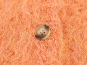 Detailed macro view of fuzzy orange knit texture and brown mottled button on a vest