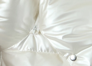 Detail of pearl white quilted jacket featuring glossy fabric and silver metallic snap button