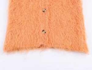 Detail of peach fuzzy knit vest with marble buttons and textured long-pile fabric
