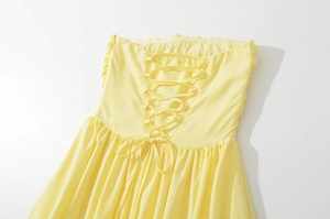 Detail of the pale yellow corset-style dress with delicate lace-up back and pleated hem