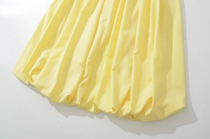 Detailed close-up of light yellow bubble hem dress with elegant pleated volume