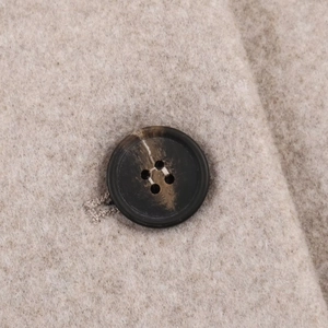Gros plan du bouton à motif marbré sur un manteau en laine beige à texture douce