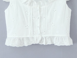 Detail eines weißen Baumwolltops mit floraler Lochstickerei und stoffbezogenen Knöpfen