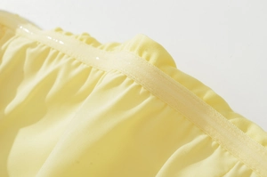 Detailed macro shot of the elastic pleated hem and stitching on a light yellow dress