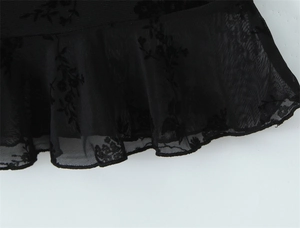 Detail of sheer black mesh fabric with floral flocking and ruffled trim edge