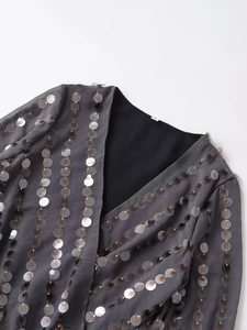 Detail of V-neck neckline with shimmering metallic sequins on dark grey fabric texture