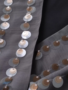 Macro detail of multi-layered sequins and studs on dark grey textured bodysuit fabric