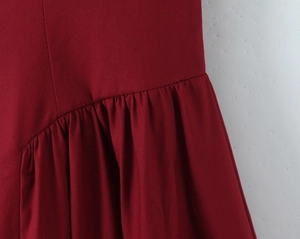 Gros plan détaillé du tissu de robe rouge foncé avec plis diagonaux et coutures soignées