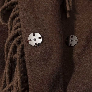 Detail of dark brown wool coat featuring silver metal snaps and woven fringe trim