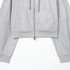 Detailed close-up of grey wool hoodie showing silver metal zipper and ribbed hem texture