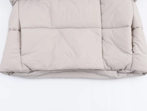 Detailed macro view of beige quilted winter jacket hem showing heavy padding and stitching