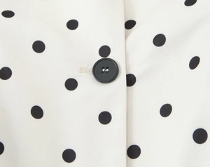 Macro shot of black button and stitched buttonhole on white polka dot blazer fabric