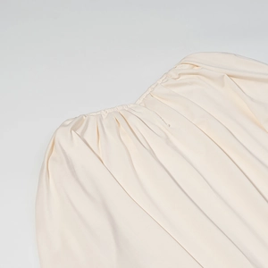 Gros plan sur les fronces élastiques et la texture plissée de la robe crème