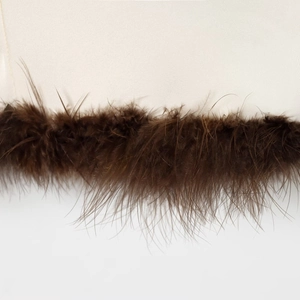 Detailed close-up of light beige fabric with premium brown feather trim and fine texture