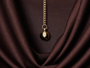 Détail d'un pendentif sphérique doré brillant sur une chaîne avec un tissu texturé