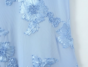 Detailed macro view of 3D ribbon flower embroidery on light blue mesh fabric material