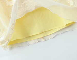 Détail de la broderie de marguerites blanches sur le tissu en maille jaune semi-transparent