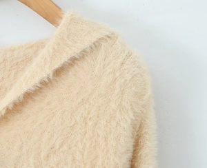 Detail shot of soft beige fuzzy knit texture and collar on a wooden hanger