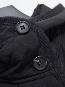 Detail of black quilted coat featuring textured resin buttons and fine woven edge trim