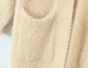 Close-up of soft beige plush knit fabric and pocket detail on a long hooded cardigan