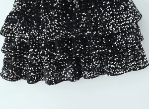 Détail d'une robe noire en maille à paillettes argentées et volants superposés