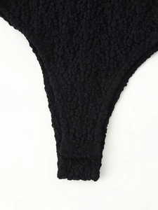Detail of black popcorn fabric bodysuit showing thick 3D bubble texture and high-cut leg