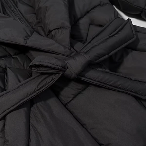 Détail d'un manteau long noir matelassé avec surpiqûres et ceinture à la taille