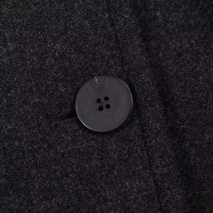 Macro detail of wool blend long coat featuring textured charcoal fabric and a matte button