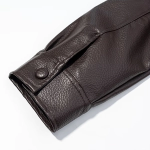 Detail of dark brown leather jacket cuff featuring a matching button and neat stitching