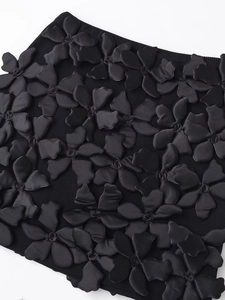 Détail du tissu à fleurs 3D noires avec pétales satinés sur une robe en maille chic