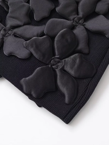 Détail de maille côtelée noire avec fleurs 3D en satin brillant sur la robe courte
