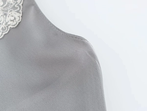 Dettaglio del tessuto satinato grigio con bordo in pizzo bianco e cuciture di pregio