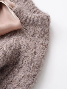Gros plan d'un pull en maille rose poudré avec fil métallique brillant et détail de ruban satin
