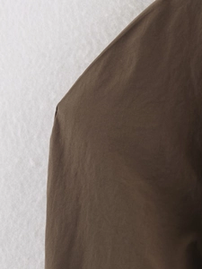 Gros plan détaillé du tissu marron foncé du trench avec une texture mate subtilement plissée