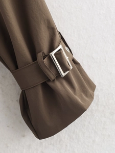 Détail du poignet d'un trench-coat marron foncé avec sangle réglable et boucle en métal