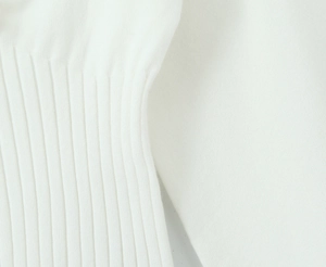 Gros plan détaillé montrant la texture en maille côtelée douce de ce pull blanc à manches