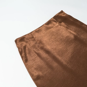Dettaglio del tessuto in raso marrone scuro con texture liscia e finitura perlata