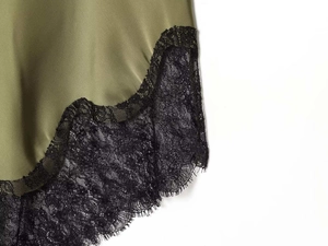 Detailed close-up of olive green satin fabric with delicate black lace trim on the hemline