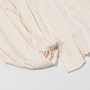 Détail macro montrant la couture surjetée fine sur le tissu en maille beige de la robe