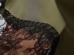 Detail of dark olive green satin fabric and intricate black lace trim on the dress