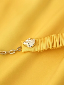 Detail of yellow satin fabric with gold irregular buckle and chain strap accent