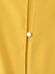 Macro view of bright ginger yellow satin midi dress featuring a gold button detail