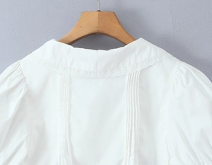 Détail de la blouse blanche avec bords en dentelle et plis sophistiqués au dos