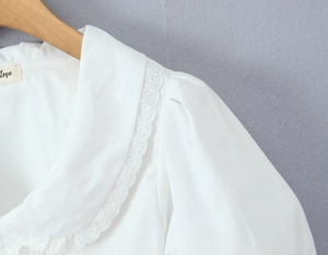 Détail d'un haut en coton blanc avec col Claudine en dentelle et manches bouffantes