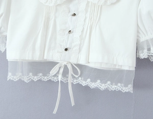 Détail du haut blanc avec col en dentelle, tissu plissé et broderie florale à l'ourlet