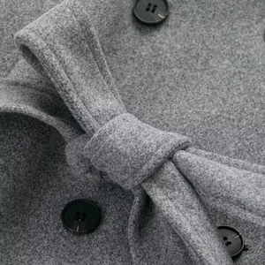 Detailed close-up of grey wool blend coat featuring a tied waist belt and black buttons